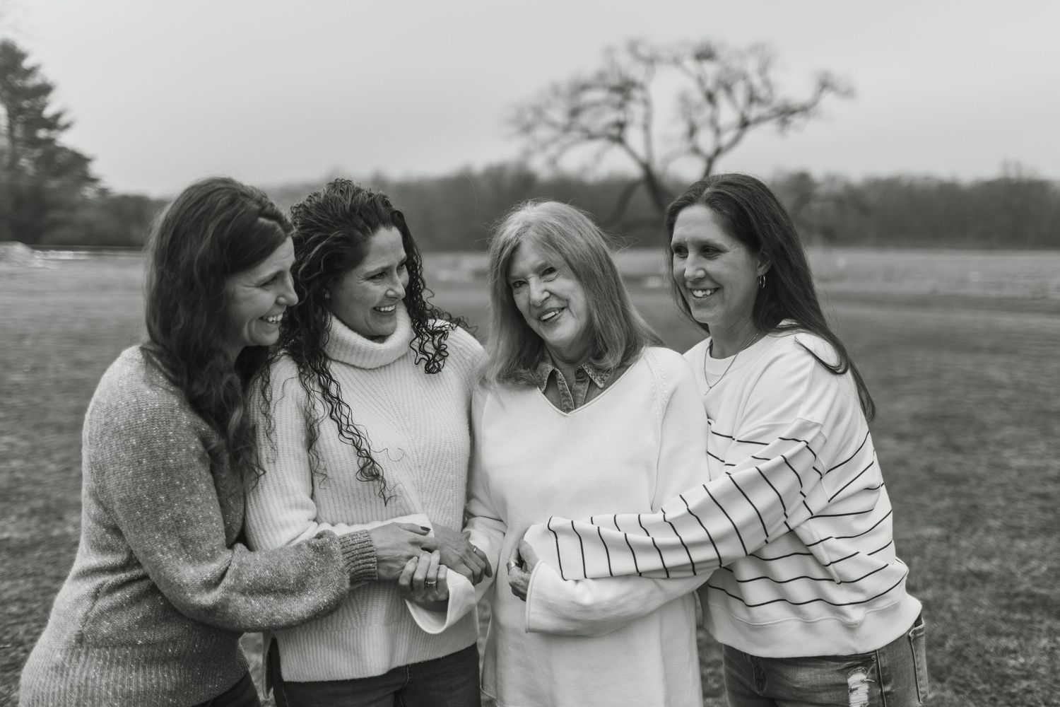 Black and white photo of four friends sharing joyful moment outdoors.