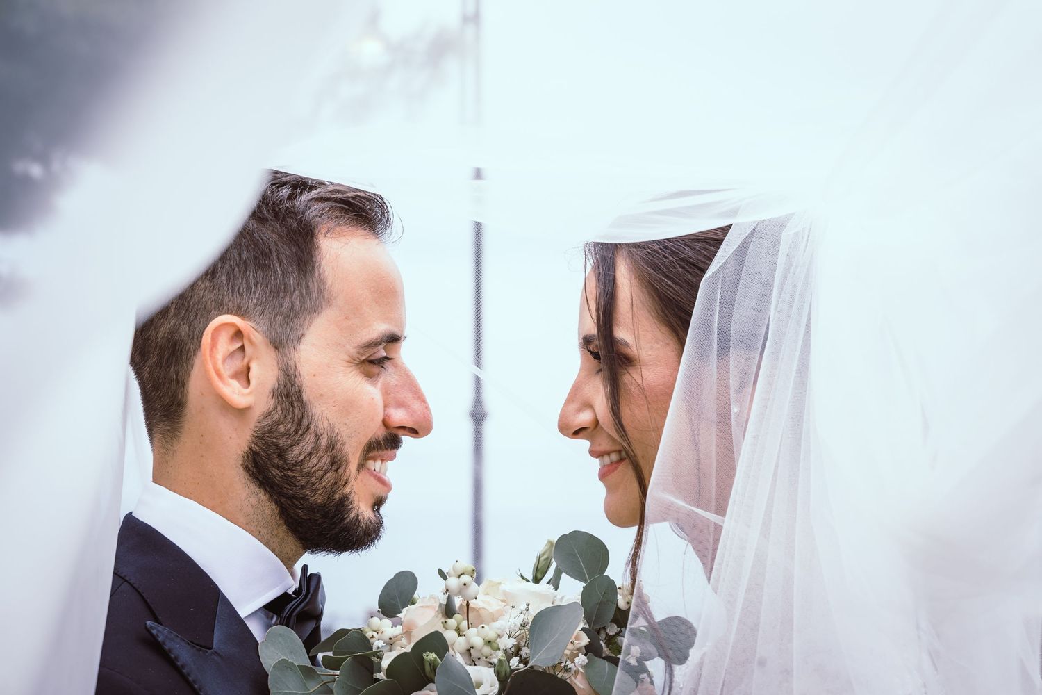 Intimate wedding portrait of newlywed couple sharing romantic moment with bride in white veil.