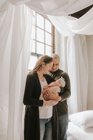 Intimate family portrait with newborn against white curtained windows.