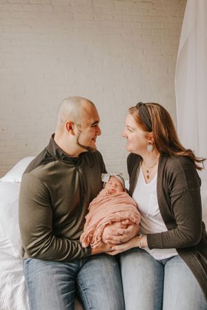 Candid family moment on white couch with newborn wrapped in peach swaddle.