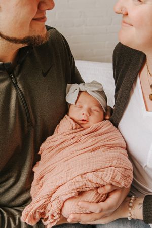 Close-up of sleeping newborn wrapped in peach muslin being held by parents.