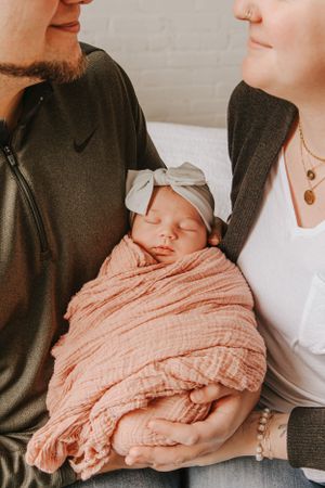 Parents hold their newborn baby wrapped in a soft pink blanket in a series of tender moments.