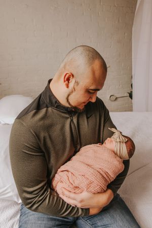 Parent gently holds sleeping newborn wrapped in pink blanket while sitting on white couch.