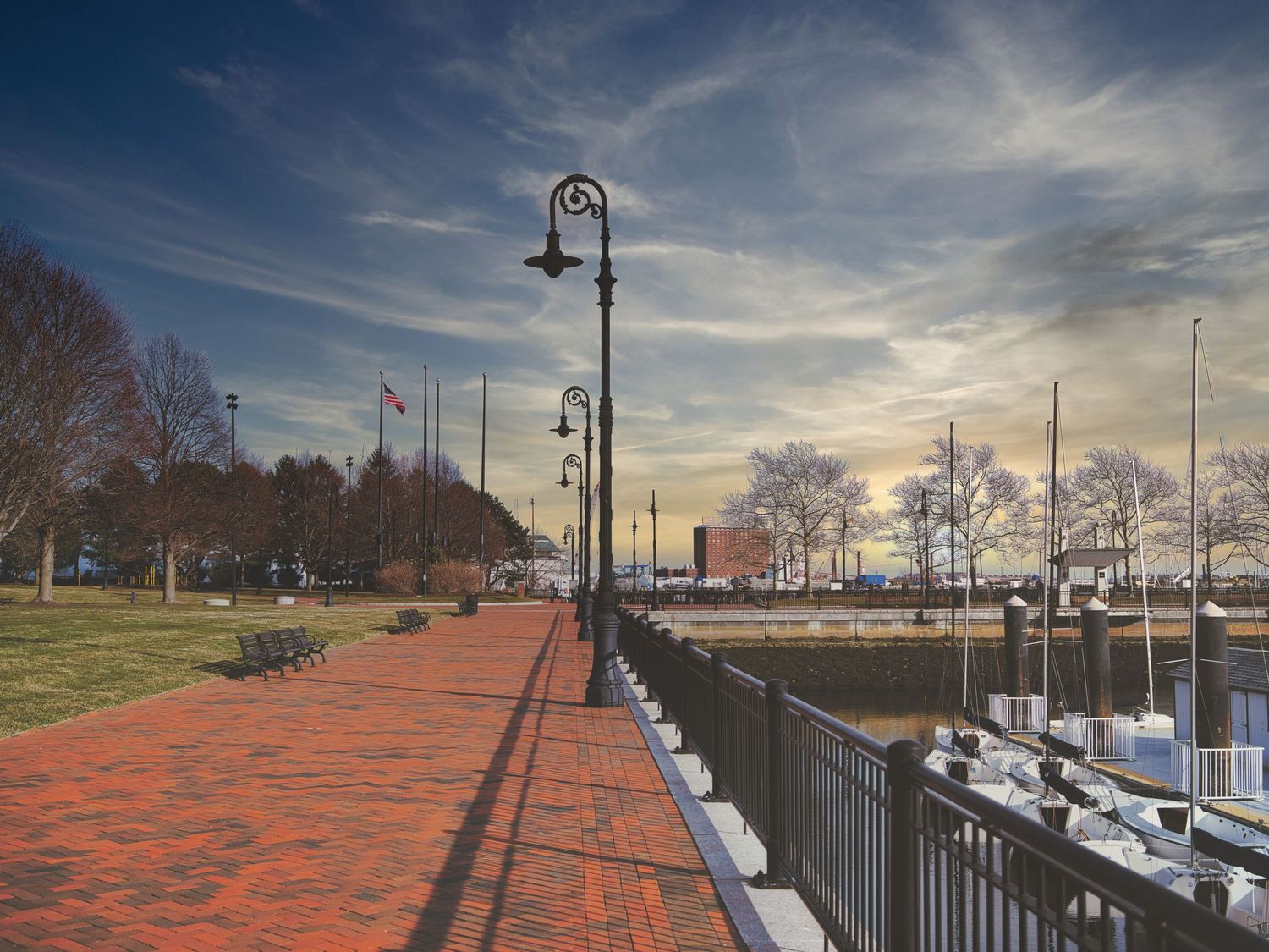 Historic brick waterfront promenade with ornate lamp posts and iron fence at sunset.