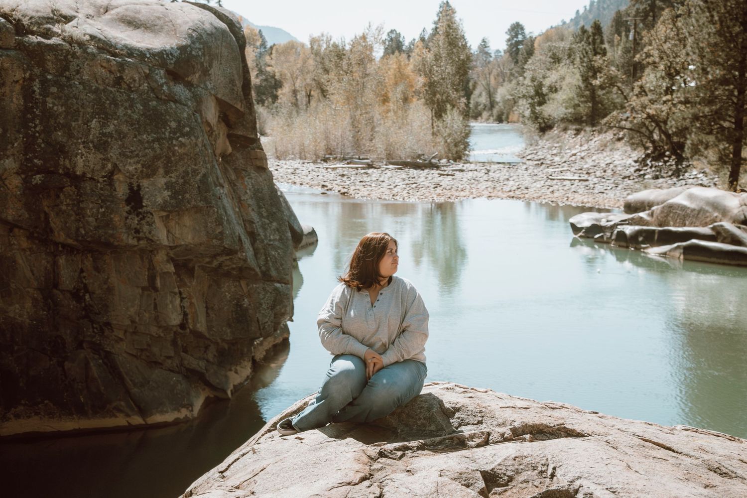 A tranquil scene of someone sitting on rocks by a serene blue lake surrounded by wilderness.