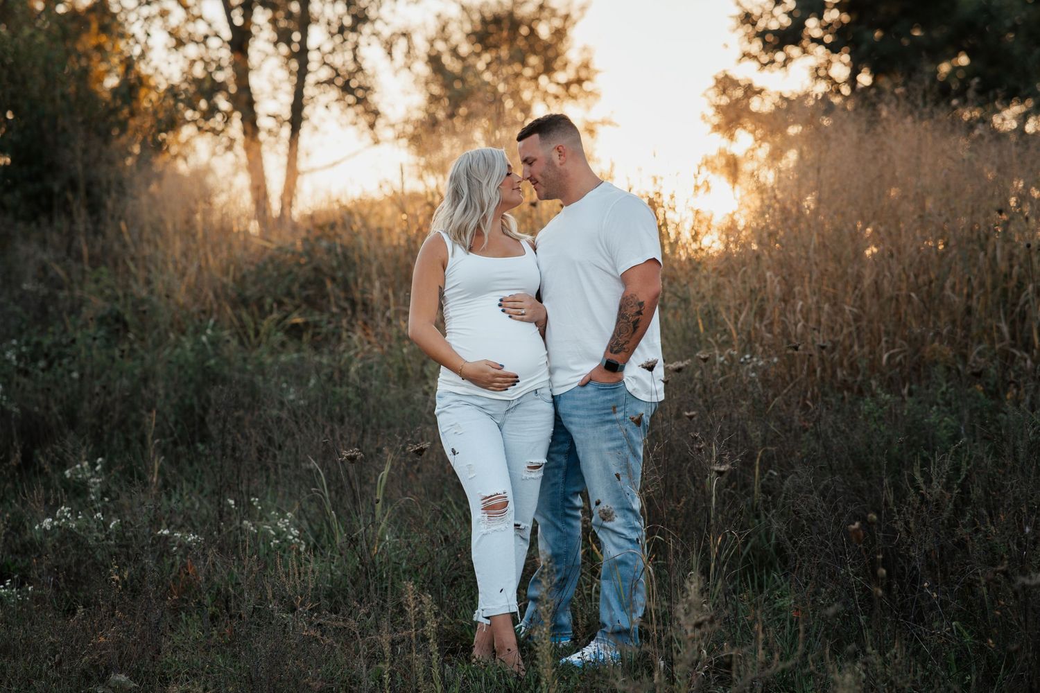 A couple shares an intimate moment in a field during golden hour.