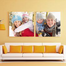 Two canvas photo prints displayed above an orange couch showing winter scenes with warm clothing and scarves.