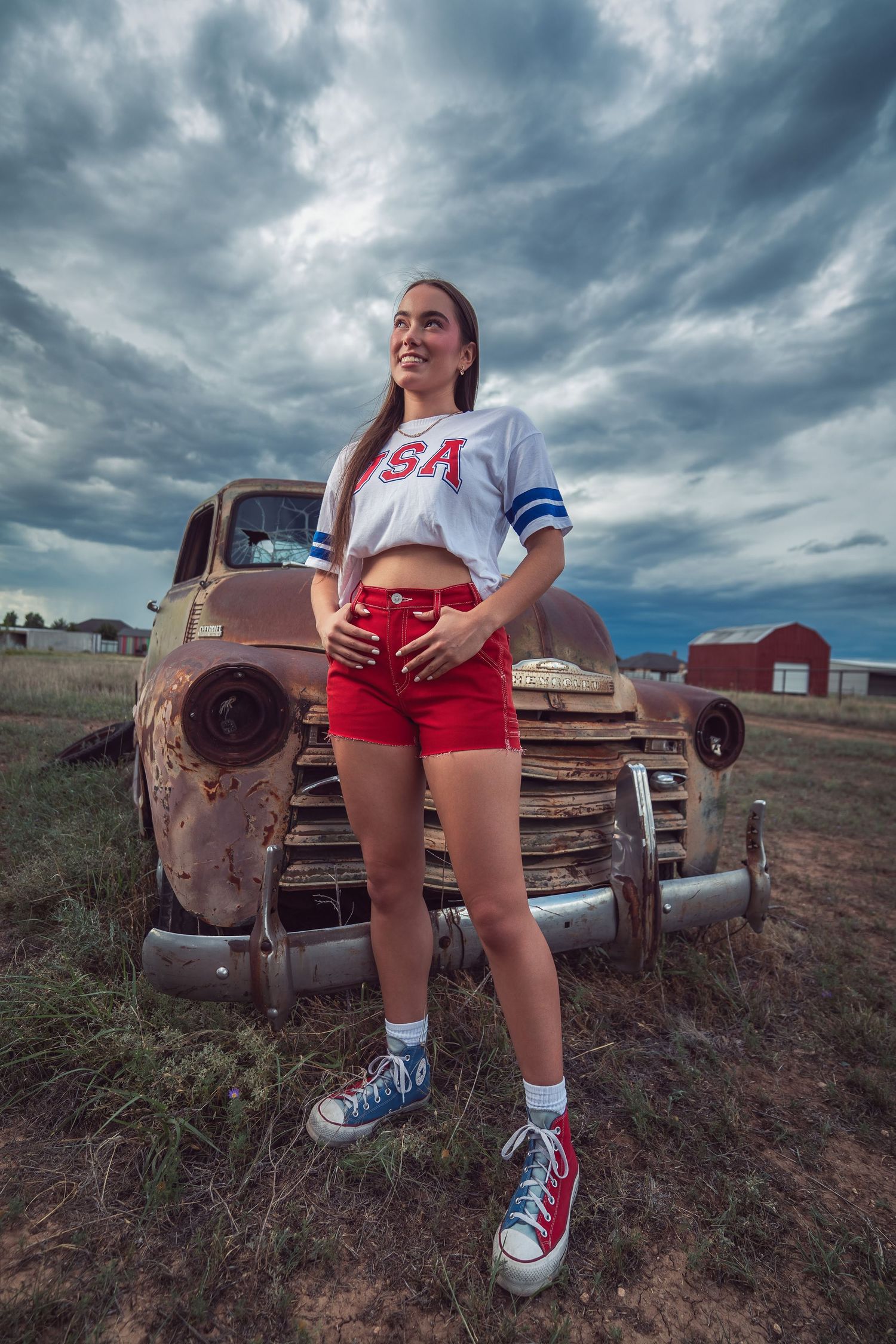 A retro-styled photo with a USA-themed outfit posed against a vintage rusty truck under dramatic storm clouds.
