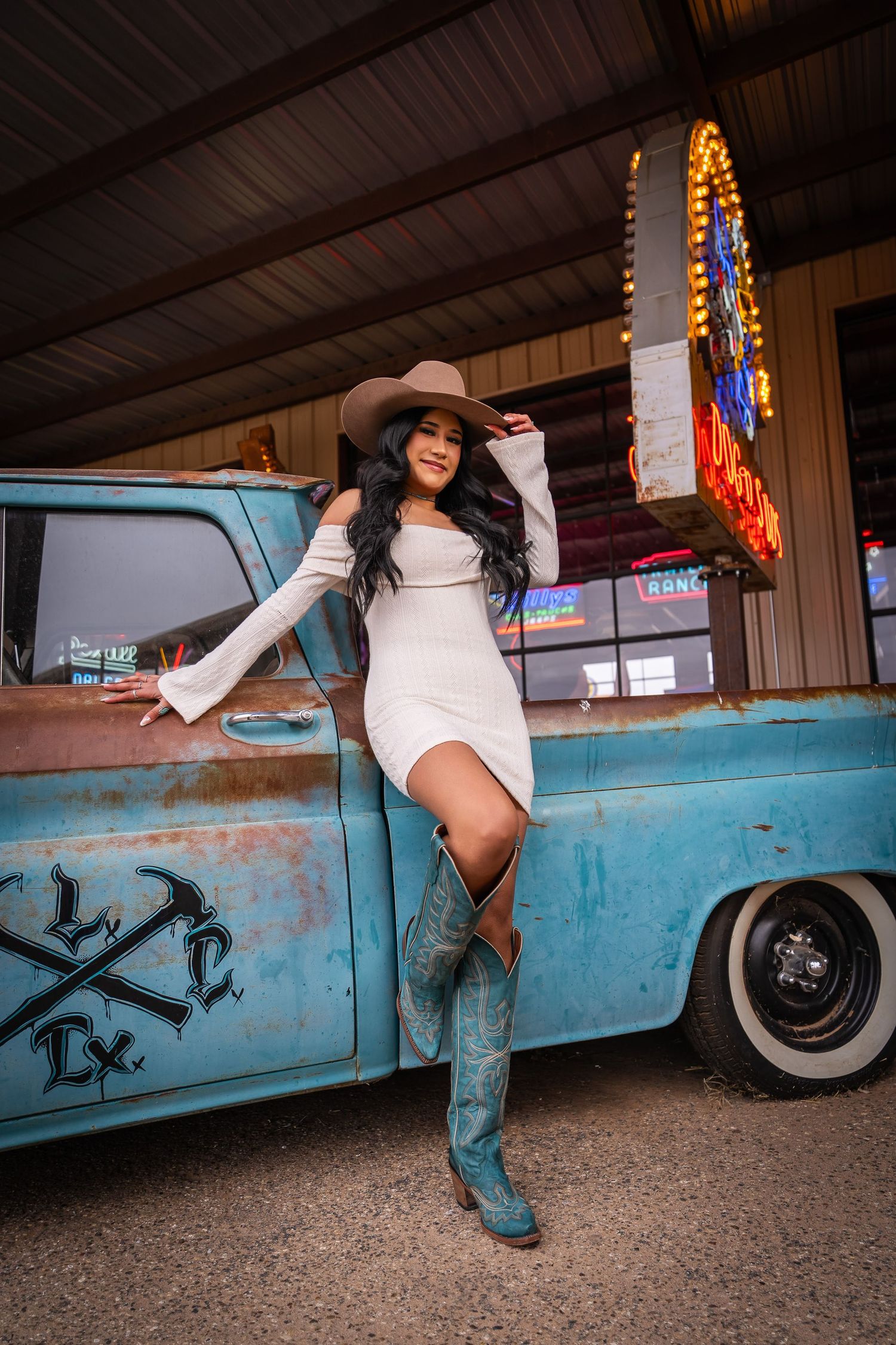 A country-western styled scene with a vintage blue pickup truck and neon sign in the background.