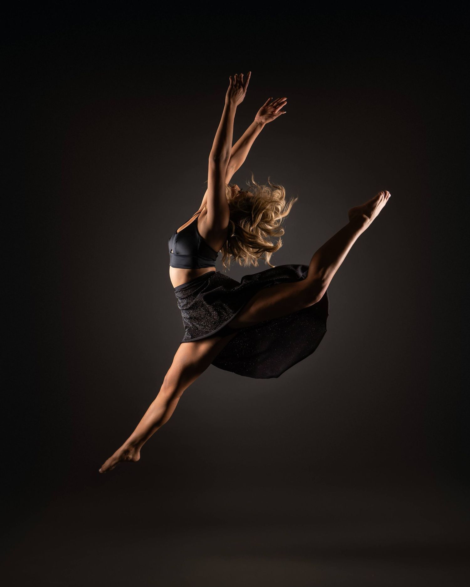Graceful dancer in black performs dramatic leaps and poses against dark background in artistic dance photo series.