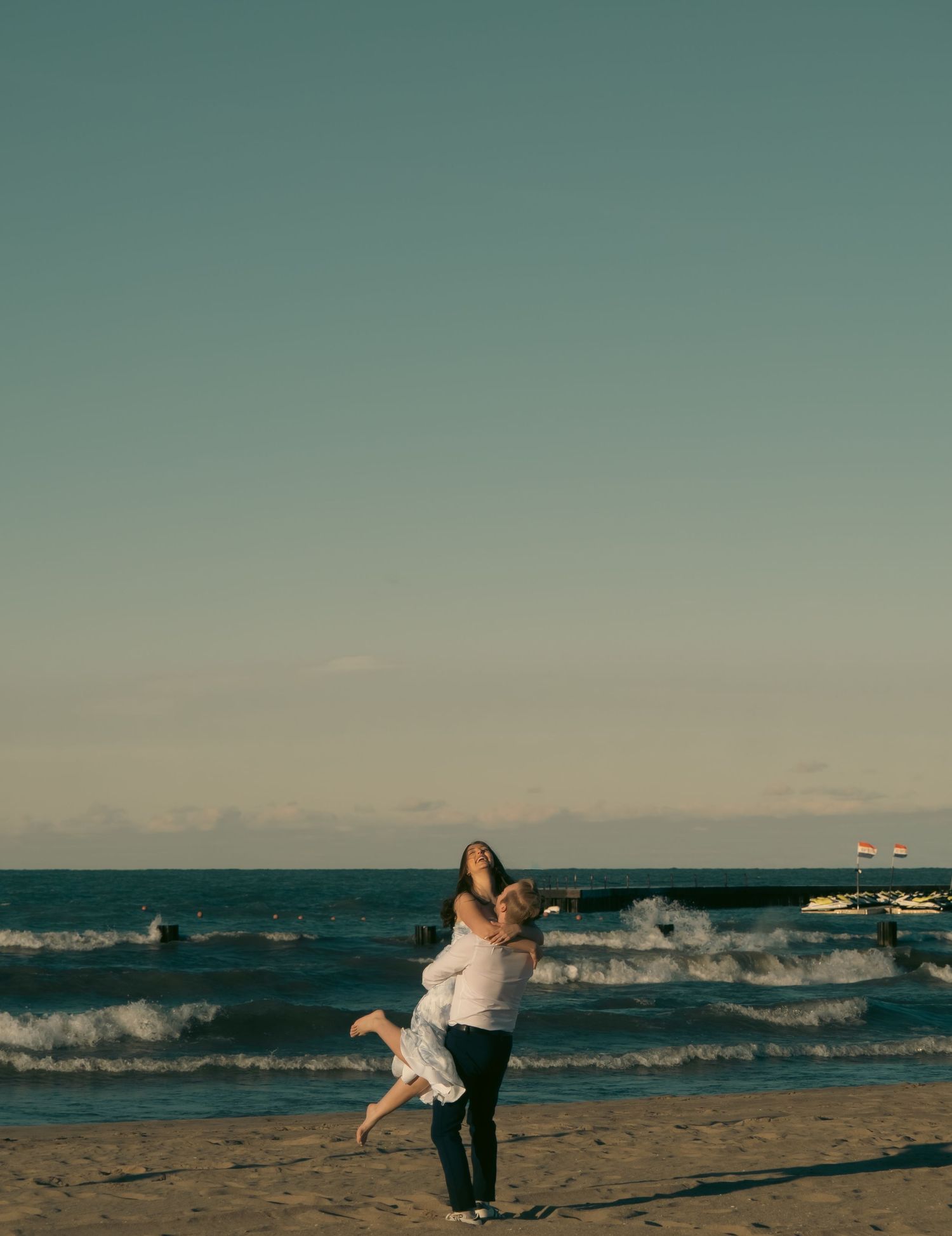 A joyful couple embraces on a beach with waves crashing in the background.