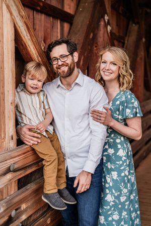 A family poses together against a rustic wooden barn backdrop while wearing coordinated casual attire.