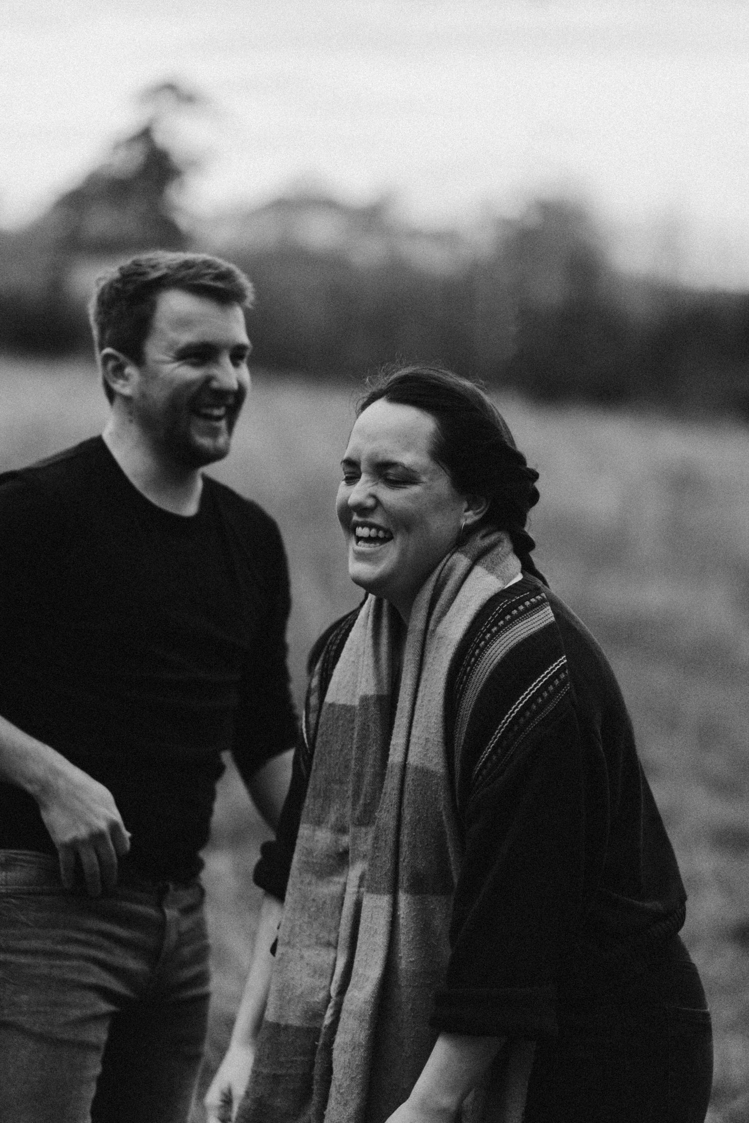 A couple shares a candid laughing moment together in black and white photography.
