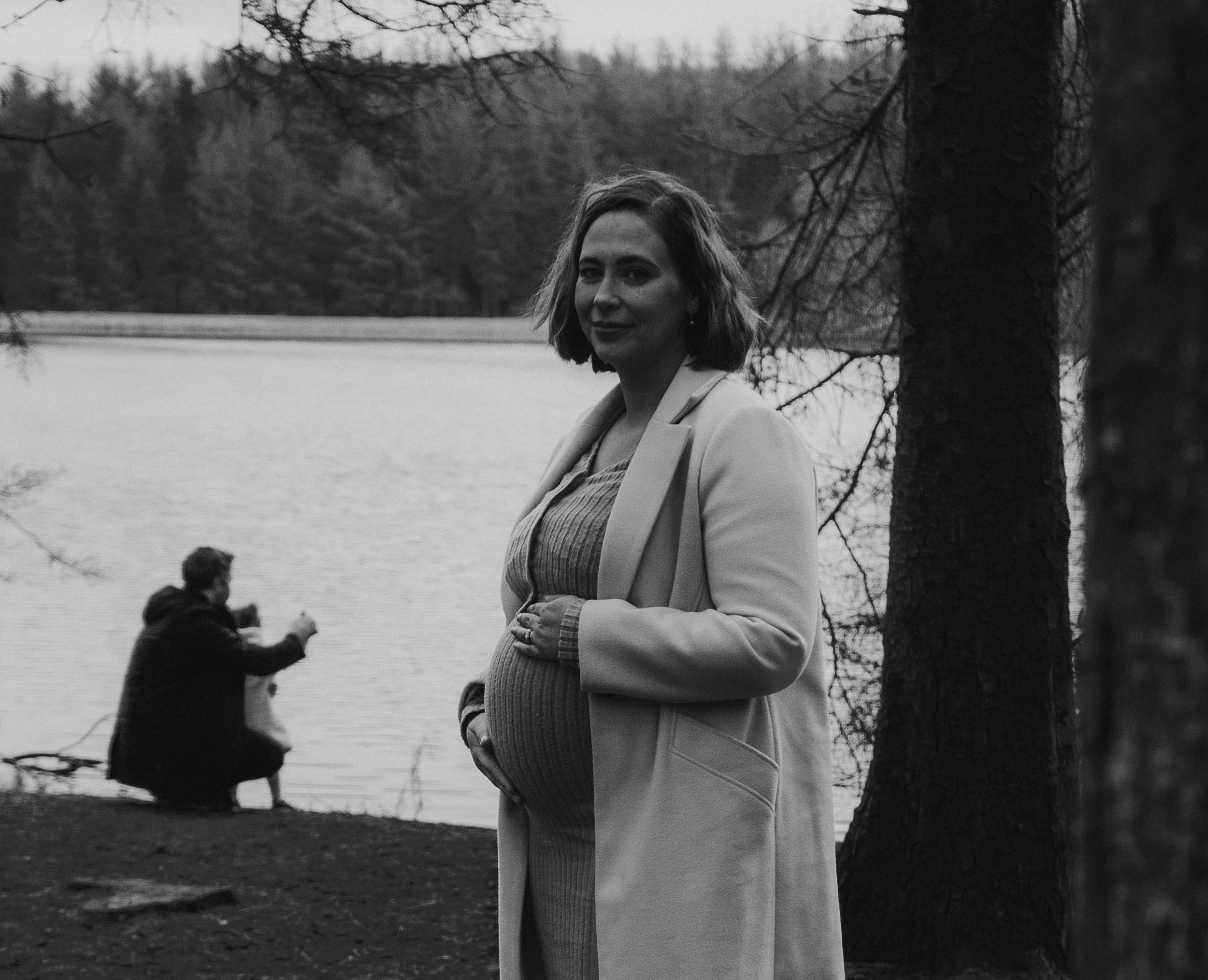 Showing off bump with husband and child playing in background