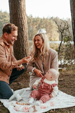 Family enjoying playful moments on a white blanket under tall pine trees in an outdoor forest setting.