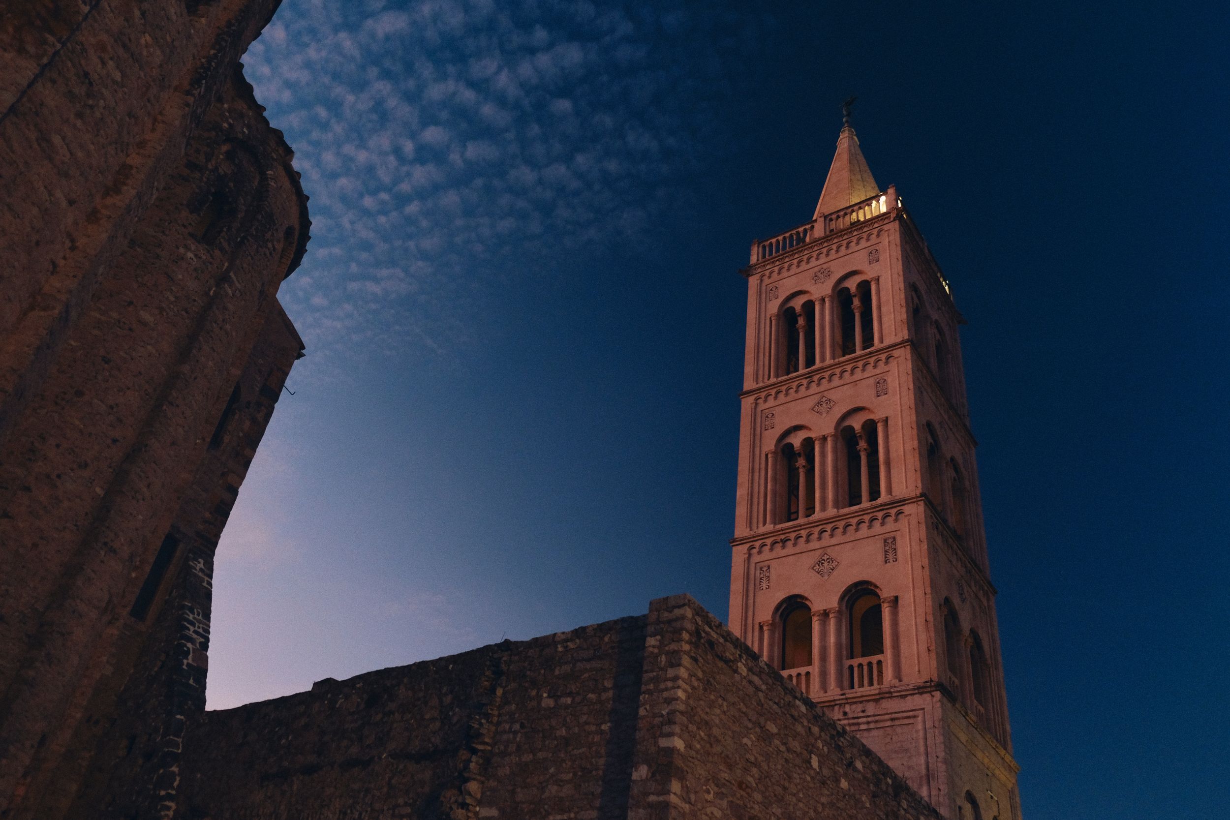 Ancient stone bell tower against deep blue sky with textured clouds.