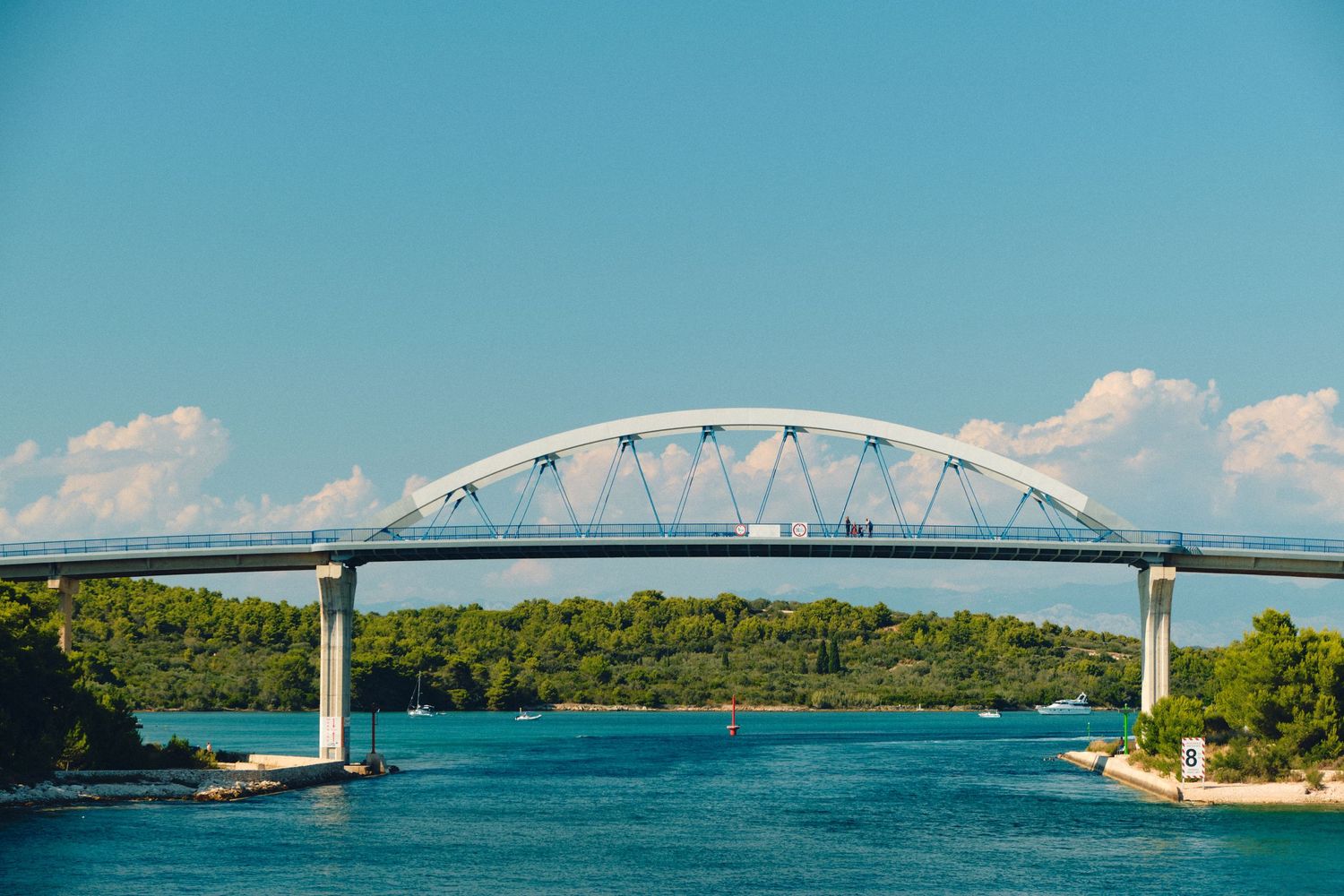 White arched bridge spanning across blue water connecting two green shorelines.