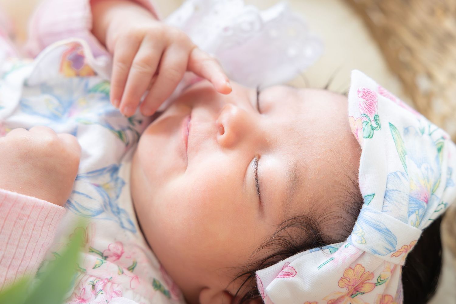 Peaceful newborn baby sleeping wrapped in a floral blanket with delicate features and dark hair.
