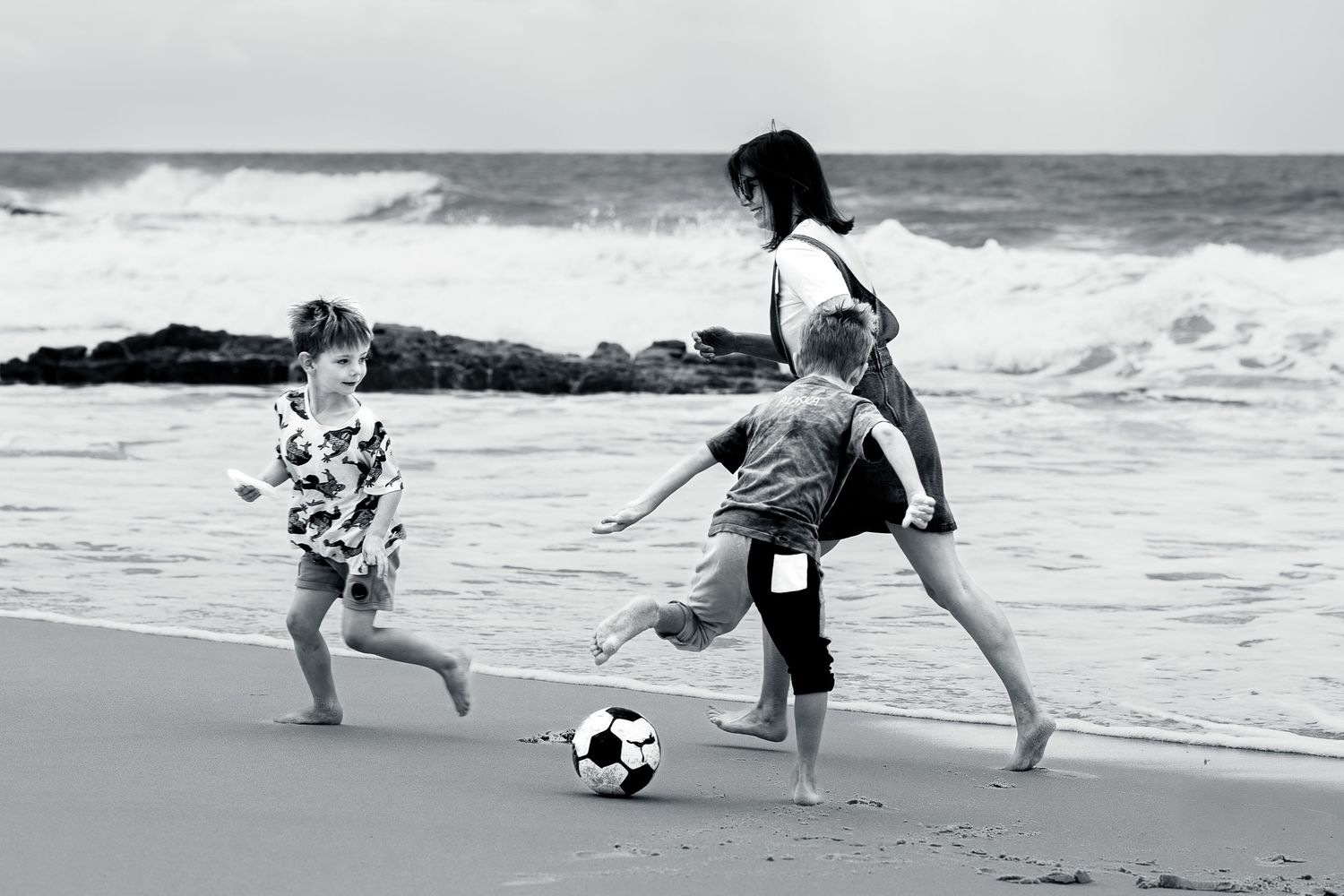 A sequence of black and white photos showing people practicing martial arts moves on a beach with crashing waves.
