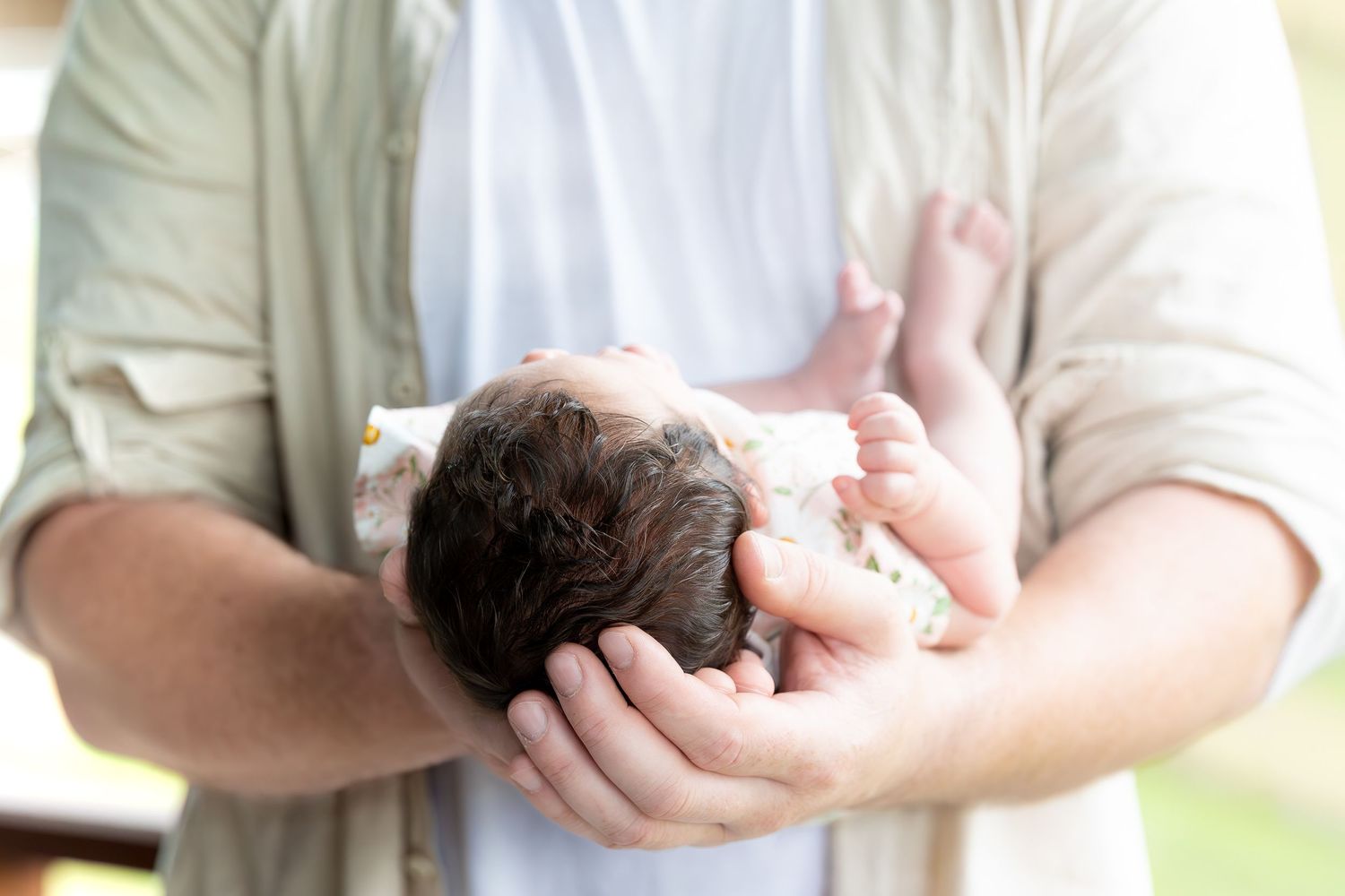 A series of hands holding newborn babies swaddled in white blankets against soft neutral backgrounds.