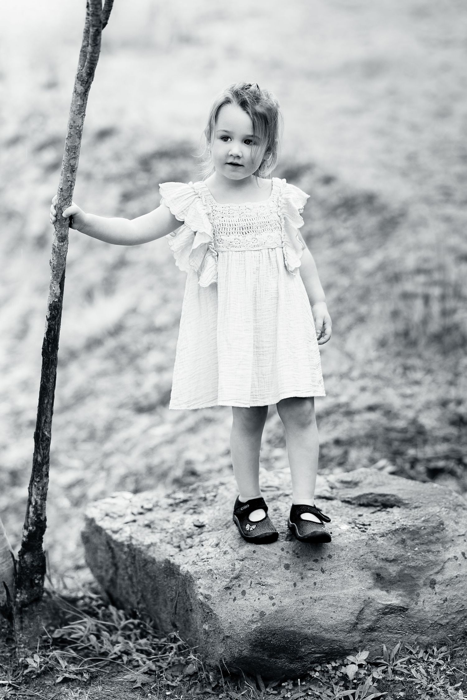 A series of black and white photos showing a small child in a white dress standing on rocky ground.