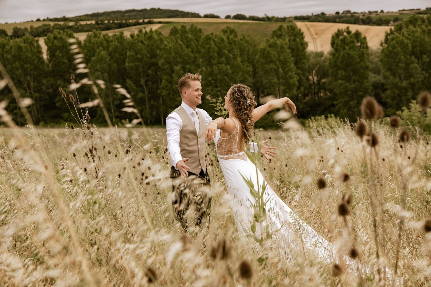 A couple walks through a scenic field of tall grass and wildflowers during a romantic outdoor photo session.