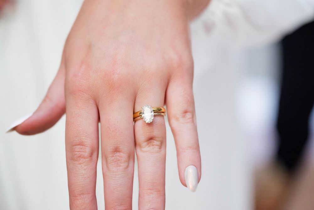 Close-up of a hand wearing an elegant gold engagement ring with neutral manicured nails.