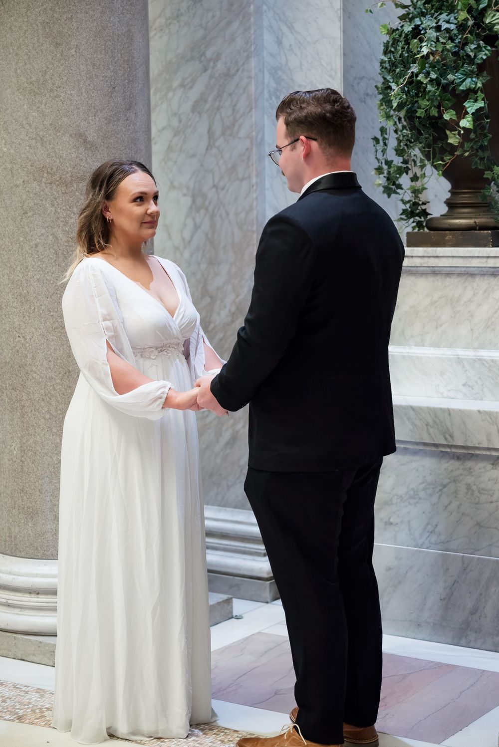 Wedding sequence showing couple in white dress and black suit interacting in front of marble columns.