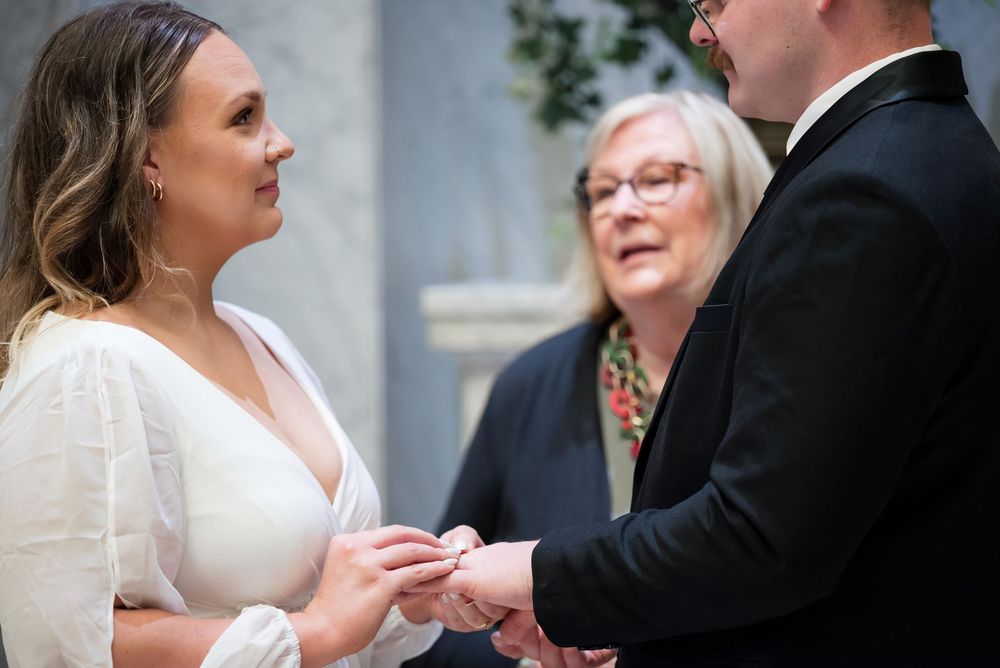 Couple exchanging rings during intimate wedding ceremony with officiant present.