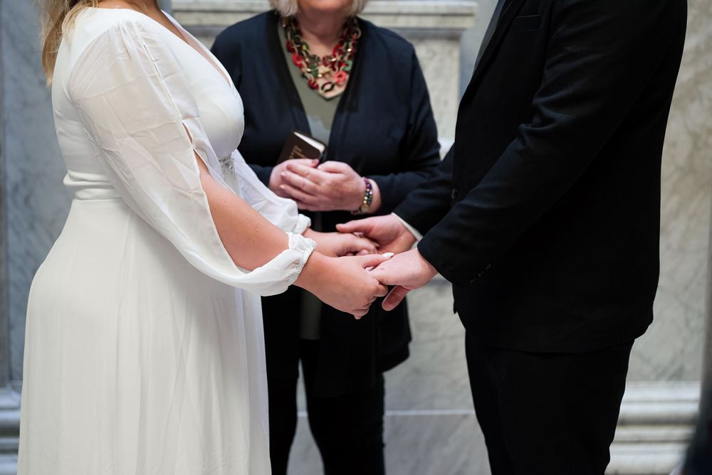 Close-up of wedding ring exchange between bride in white dress and groom in black suit.