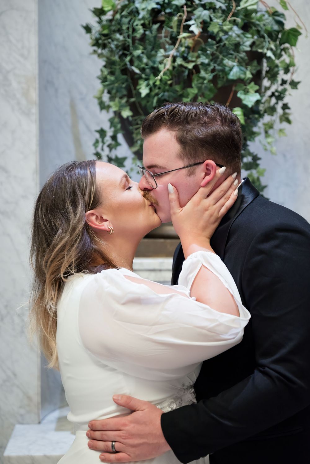 Romantic kiss sequence between newlyweds against ivy-covered wall background.