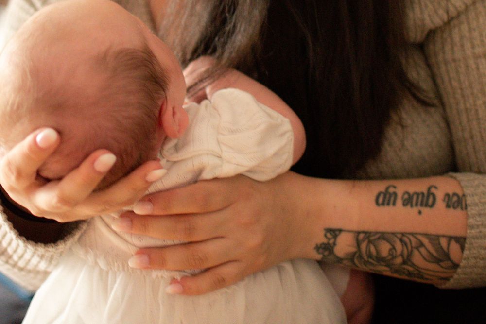 Tattooed mother tenderly cradling and breastfeeding her newborn baby, with a never give up tattoo visible.