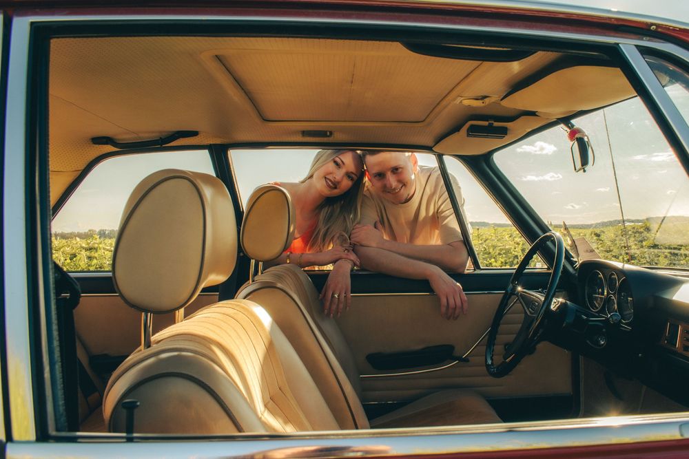 Couple relaxing inside a vintage car with beige interior, golden sunlight streaming through the windows.