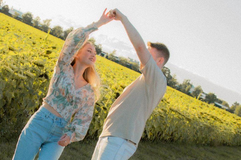 A joyful couple dancing together in a sunny green field, the woman spinning with arms raised.