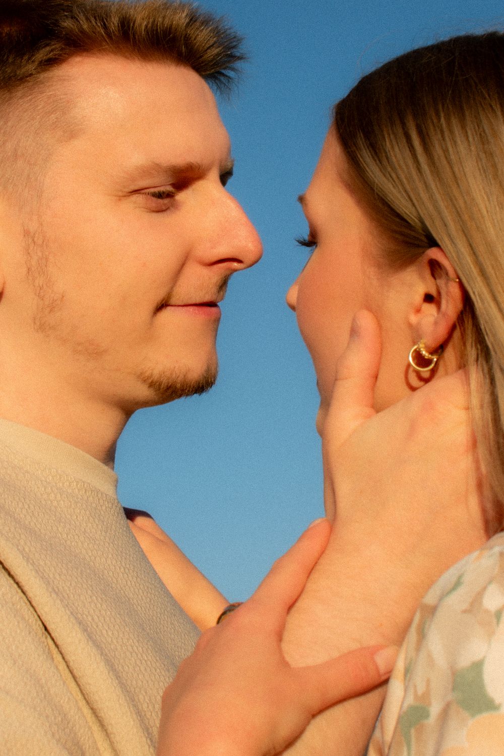 Romantic couple sharing a tender moment outdoors, man gently holding woman's face against a blue sky backdrop.