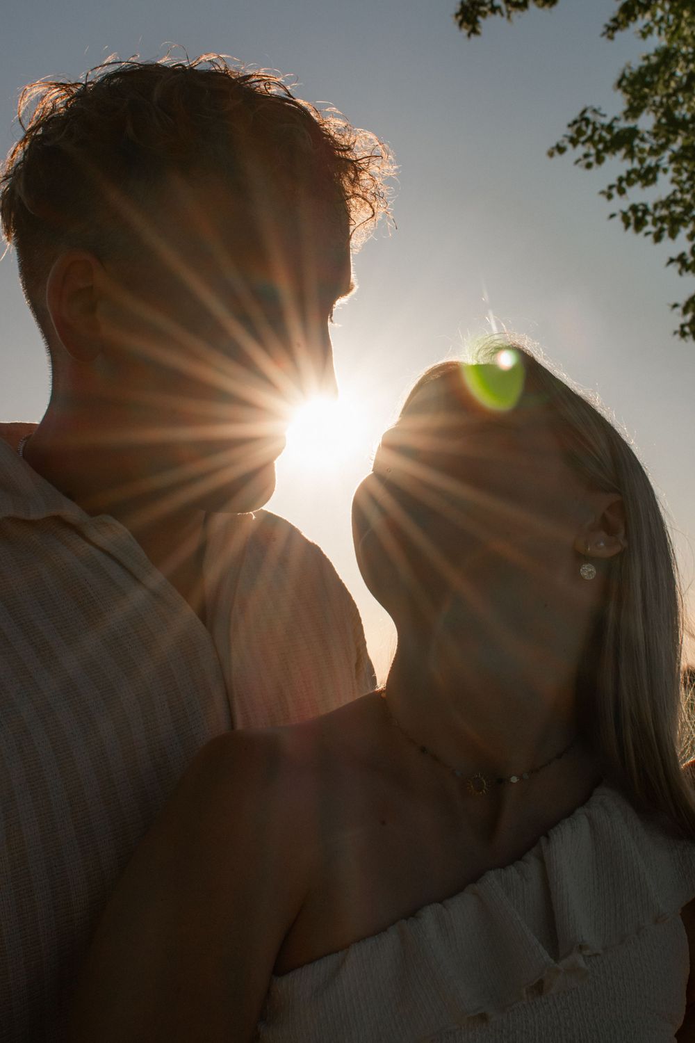 Romantic couple silhouetted against golden sunset with sun rays streaming between them outdoors.