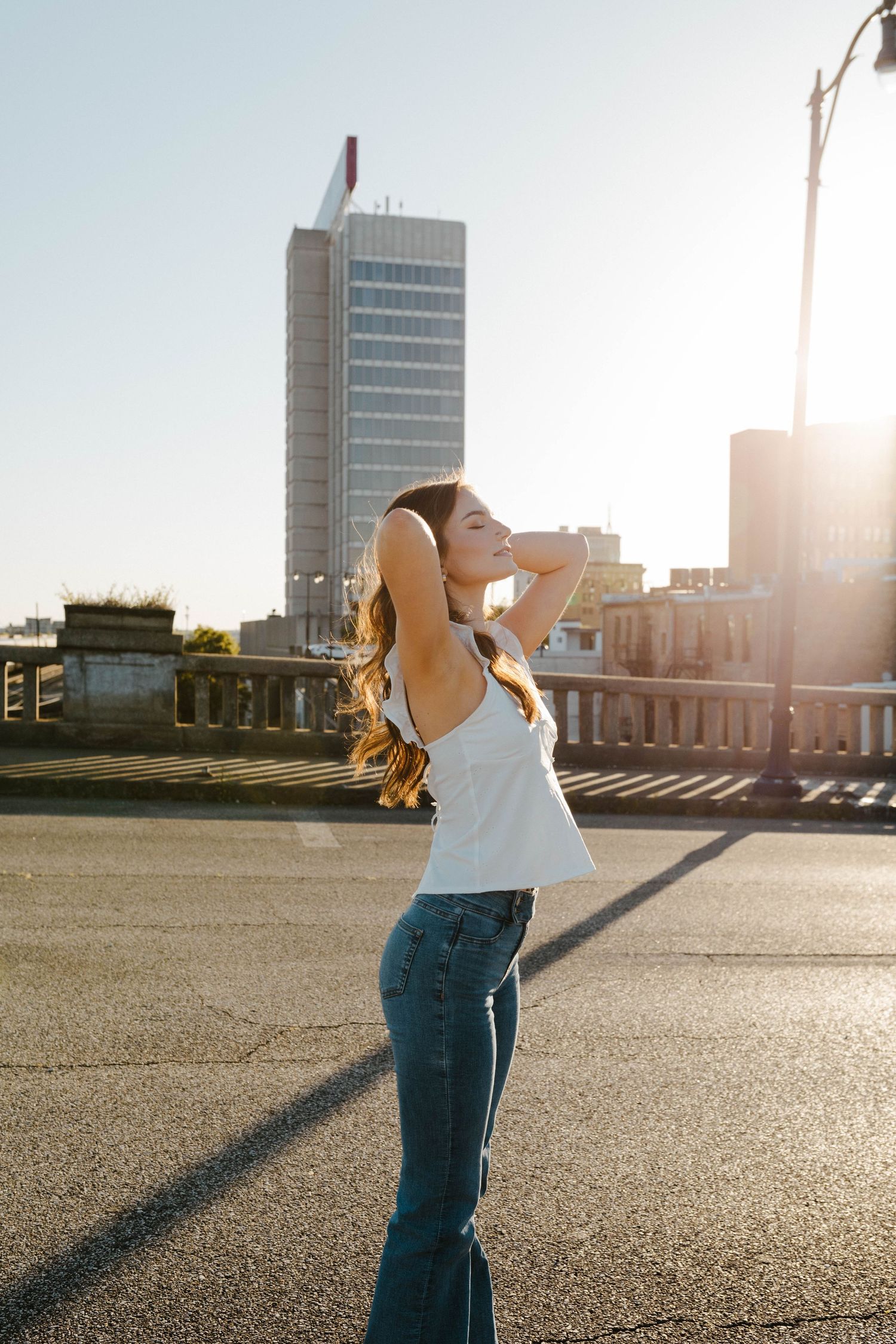 Woman in casual attire enjoying sunlight on urban rooftop with city buildings in background.