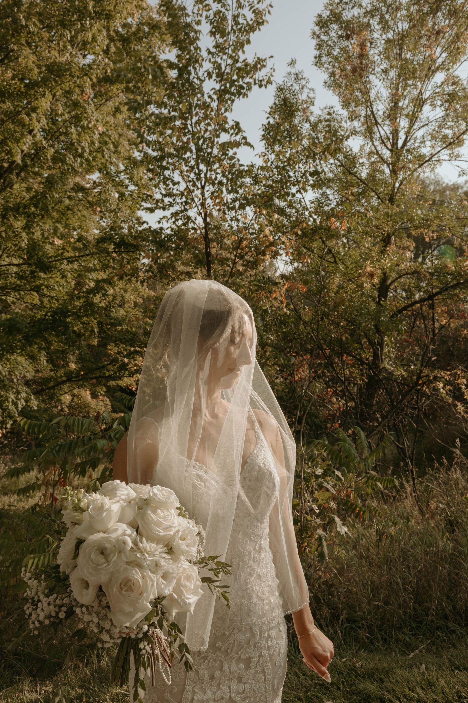 A close-up detail of a white lace wedding dress train draped elegantly on grass during an outdoor ceremony.