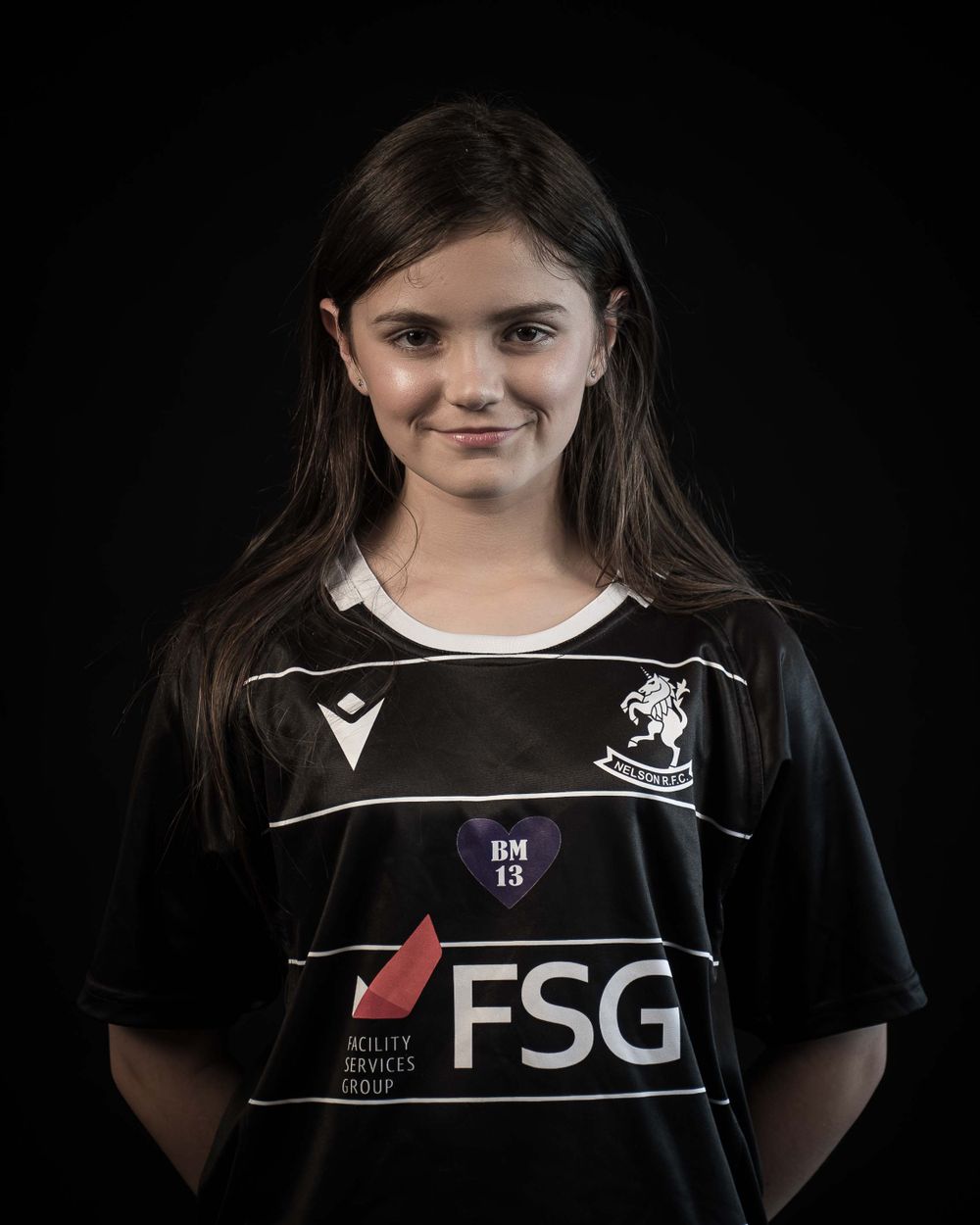 Player in black FSG-sponsored jersey poses for team photo against dark backdrop.