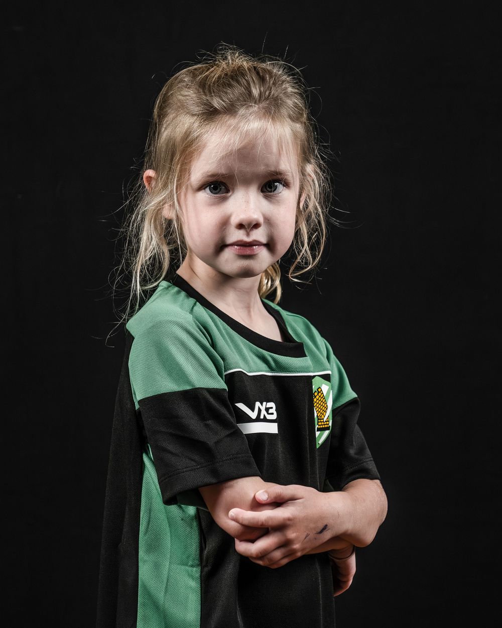Studio portraits against black background showing youth sports player in green and black uniform.