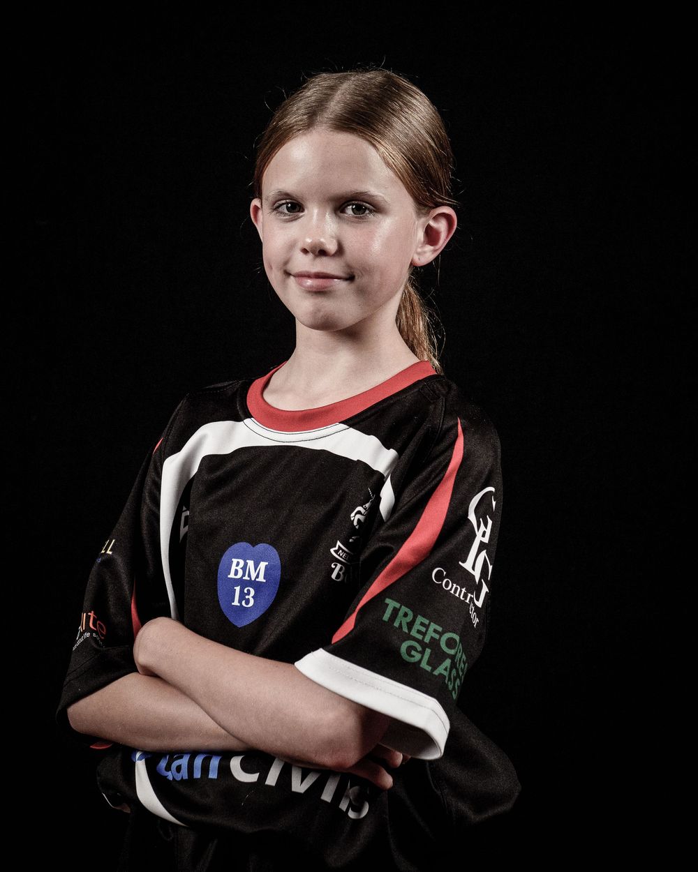 Studio portraits against dark background showing youth sports player in black uniform with red accents.