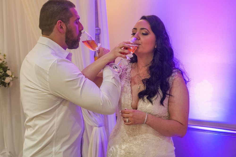 Wedding couple feeds each other cake at their reception under purple lighting.