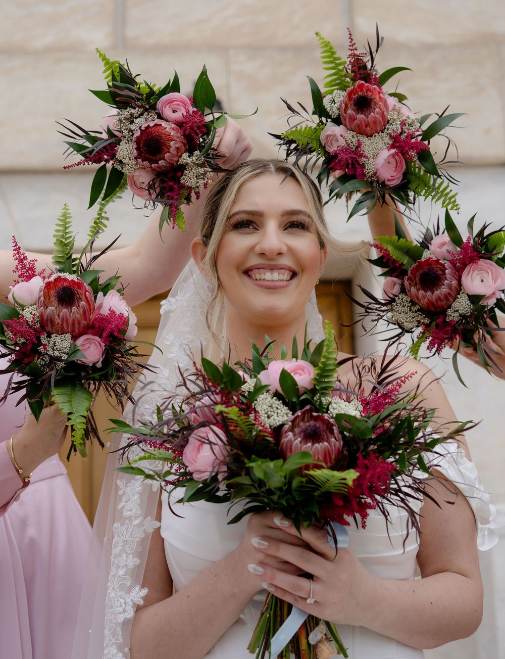 Bridesmaids holding vibrant pink and burgundy floral bouquets.