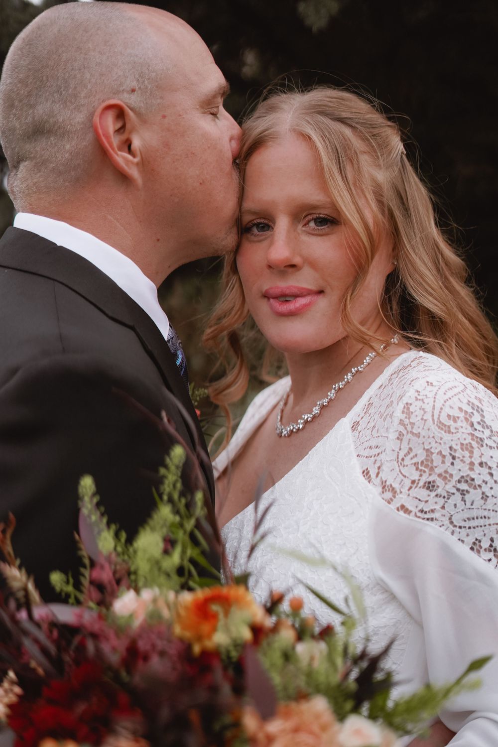 Wedding couple shares intimate moment surrounded by colorful floral arrangements.