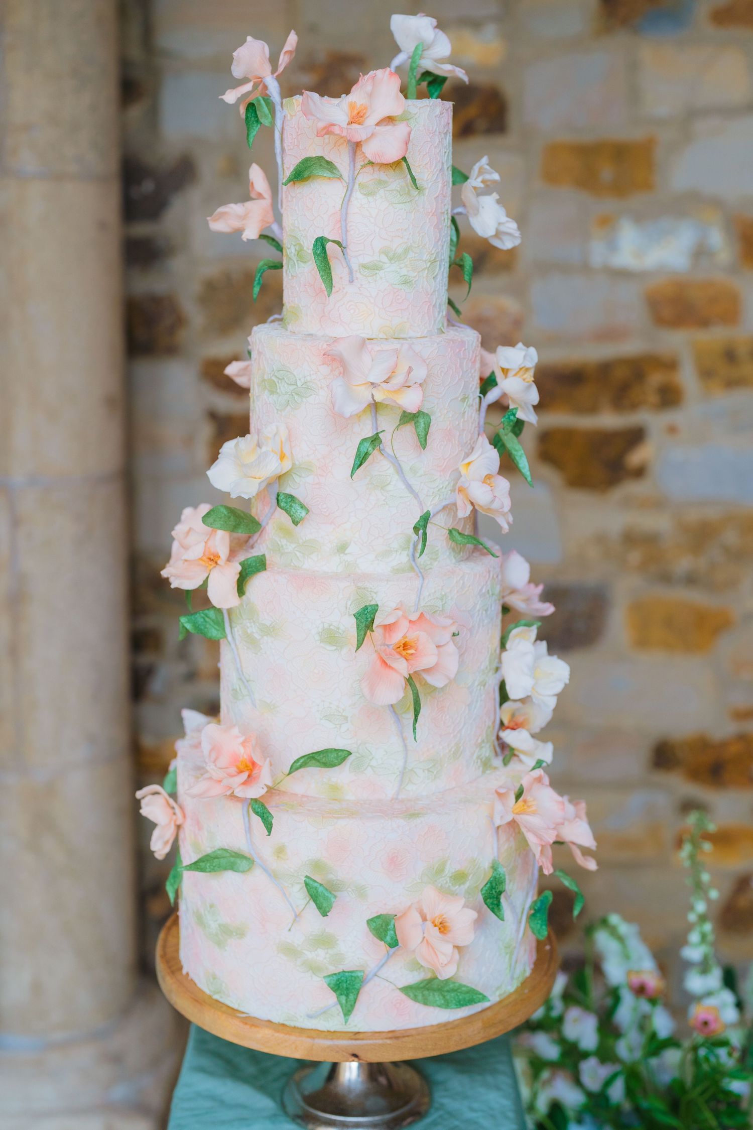 Elegant three-tier wedding cake decorated with pink sugar flowers and green leaves.