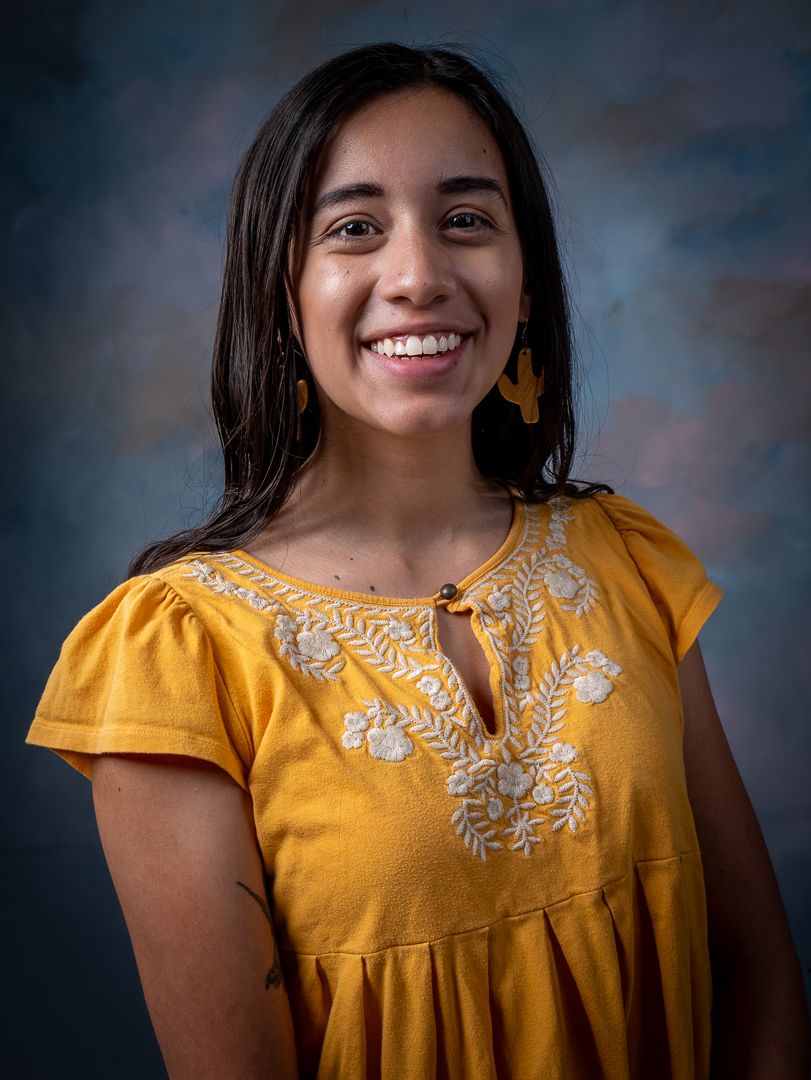 Studio portrait of a person wearing a yellow embroidered dress against blue background.
