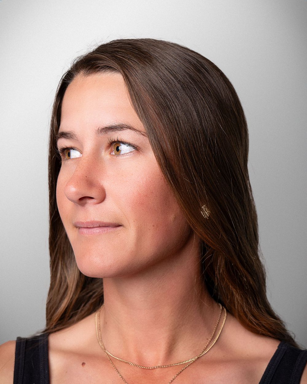 Side profile studio portrait showing long brown hair and subtle smile against neutral background.