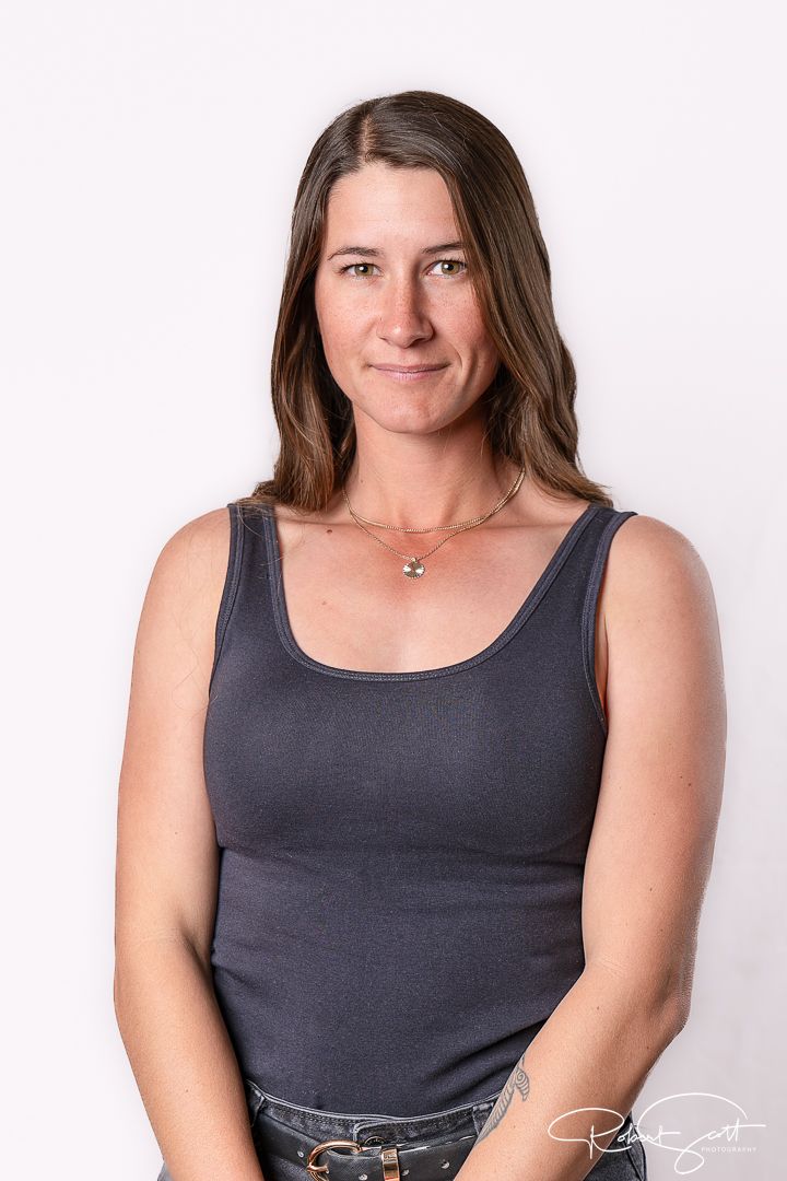Professional portrait against white backdrop wearing dark tank top and minimalist jewelry.