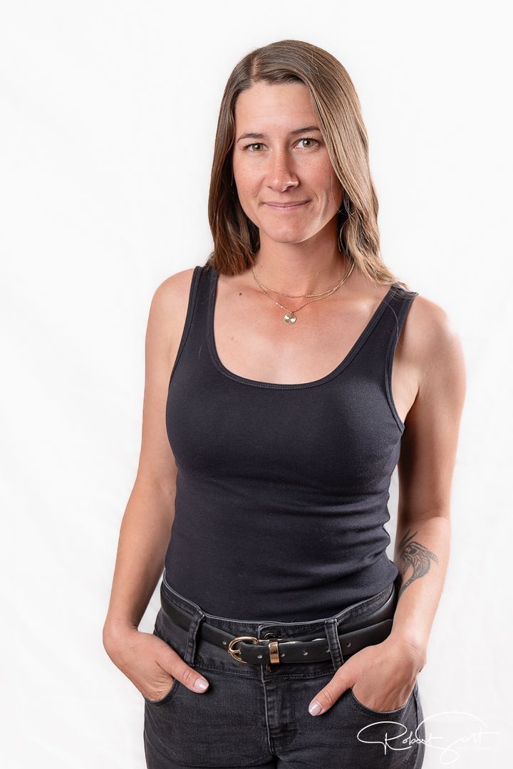 Casual portrait in black tank top and jeans with hands in pockets against white background.