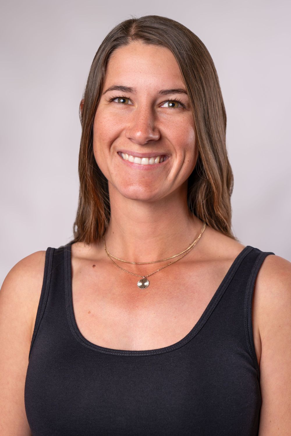 Cheerful studio portrait in black sleeveless top with delicate jewelry against light backdrop.